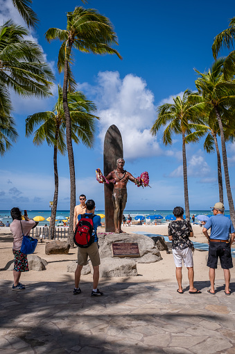 Honolulu, HI - April 29, 2022: Tourists taking photos of the statue along Kalakaua Avenue of the famous surfer Duke Kahanamoku.