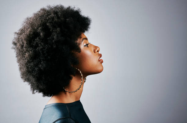 side profile of a beautiful young black woman thinking and looking powerful standing against a grey studio background. one gorgeous and serious african american female with an afro looking empowered - afro stockfoto's en -beelden