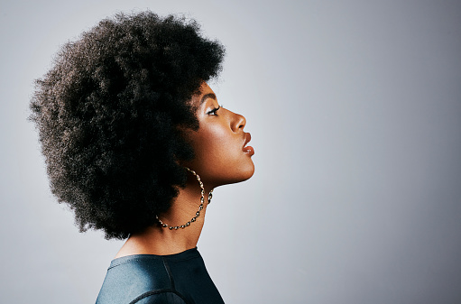Side profile of a beautiful young black woman thinking and looking powerful standing against a grey studio background. One gorgeous and serious african american female with an afro looking empowered
