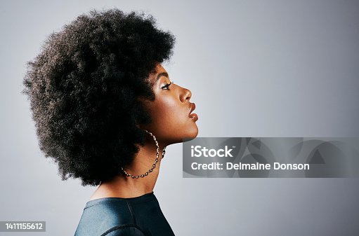 istock Side profile of a beautiful young black woman thinking and looking powerful standing against a grey studio background. One gorgeous and serious african american female with an afro looking empowered 1411155612