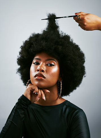 Portrait of a beautiful African lady with an afro looking at the camera with make-up on her face. Confident female with curly hair proud of her dark skin. Trendy black woman getting her hair cut