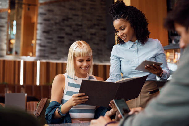 Happy black waitress recommending something from a menu to guests in a cafe.