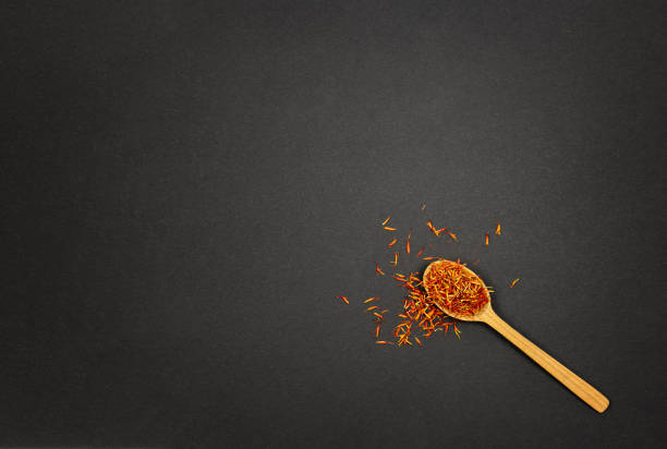 Fragrant orange saffron, Indian spice in a wooden spoon on a black background. Copy paste to the left.