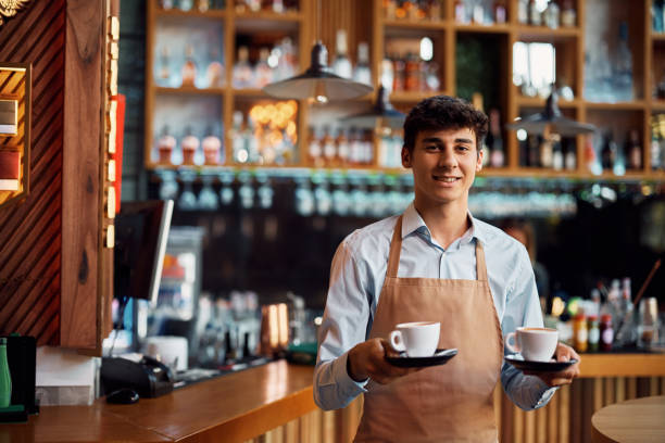 Young waiter serving coffee in a cafe and looking at camera. stock photo