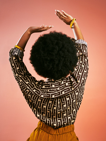 Mujer retro de moda despreocupada bailando escuchando música y divirtiéndose. Retrato desde detrás de una mujer funky y elegante con cabello afro aislado sobre un fondo marrón. photo
