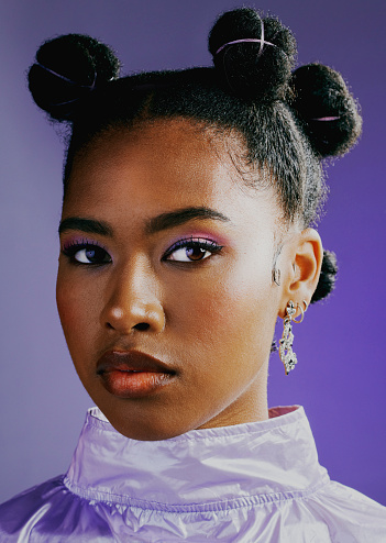 Portrait of an edgy black woman with fashionable purple makeup and retro clothes against a vibrant studio background. Confident female with bold personality, cool punk attitude and a trendy hairstyle
