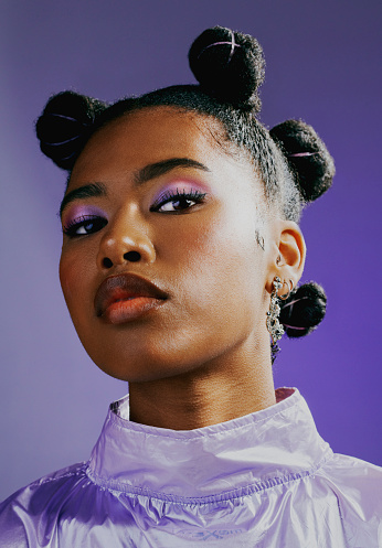 Portrait of an edgy young woman wearing fashionable purple makeup and clothes with a trendy hairstyle against a vibrant studio background. Confident female with bold personality and cool attitude