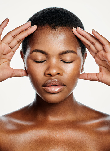 Beautiful young black woman posing against a white studio background. One female beauty model using her hands for a head massage to cure head pain. Relaxed lady feeling empowered and confident