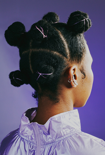 Headshot of 90s retro woman with knots hairstyle to inspire your next look. Edgy and funky girl feeling confident in purple fashion against studio background. African female with a stylish hairdo