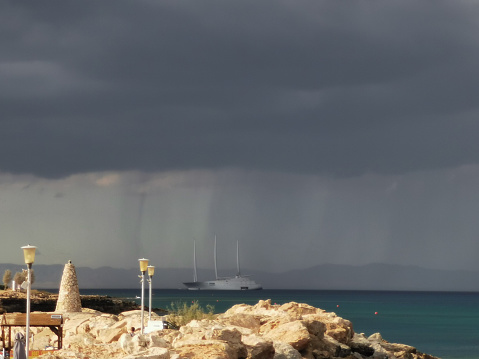 Protaras. Famagusta area. Cyprus. Large rocks on the shores of the Mediterranean Sea, dramatic skies and rain over the largest sailing yacht in the world, an eight-deck motorsailer.