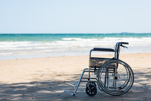 A caucasian, mature man with paraplegia, using his modified wheelchair in a nature reserve on a sunny summers day. He is wearing casual clothing and is looking out at a pond from a jetty.
