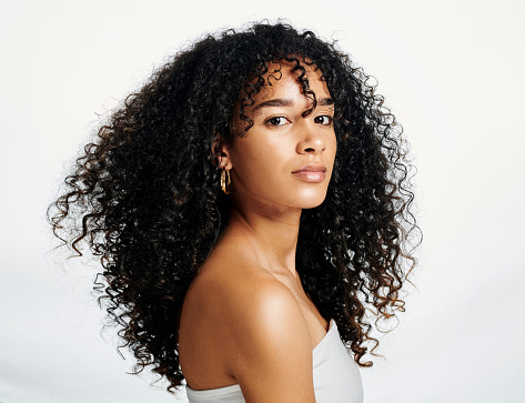 Portrait of a young beautiful black female posing against a white studio background alone. Face of one gorgeous african american woman with curly hair showing her glowing, clear complexion and skin