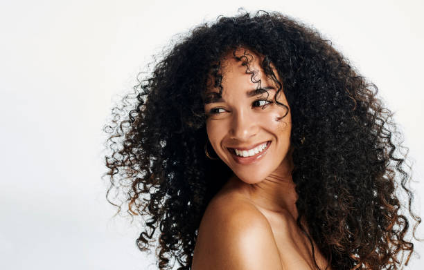 Beautiful young woman with curly hair posing against a white studio background. Confident beauty and cheerful female with glowing skin and flawless complexion feeling excited and happy Beautiful young woman with curly hair posing against a white studio background. Confident and cheerful female with glowing skin and flawless complexion feeling excited and happy while daydreaming curly hair stock pictures, royalty-free photos & images