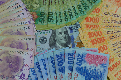 Billete de 100 dólares rodeado de billetes de peso argentino. photo
