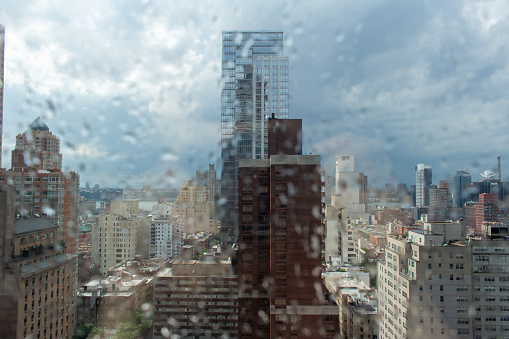 This image shows an abstract stylized texture background of defocused rain drops on a window pane with view of New York City through the glass.