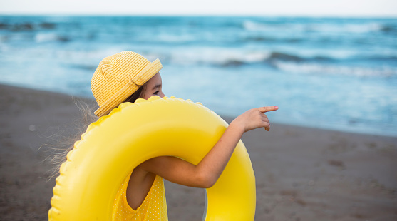 A girl with a yellow inflatable circle on the seashore. Relaxing on the beach, summer travel.