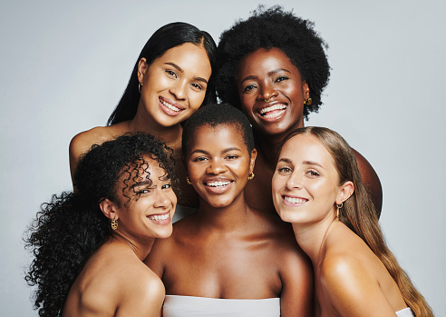 Beauty portrait of a diverse group of beautiful women smiling together against a grey studio background. Faces of female models with perfect, clear skin and complexion from a daily skincare routine