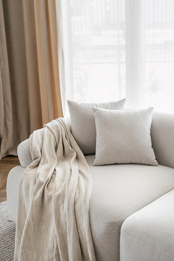 Cropped view of pillows and blanket on modern soft sofa in living room. House after renovation. Relax concept. Home comfort. Apartment interior details. Hotel room