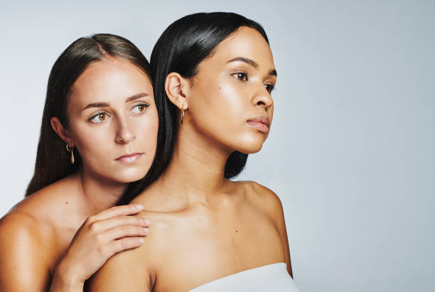 two flawless women with glowing skin isolated on studio background. face of multicultural beauty models looking confident and empowered by their natural, clean and moisturized skincare routine - blank expression head and shoulders horizontal studio shot imagens e fotografias de stock