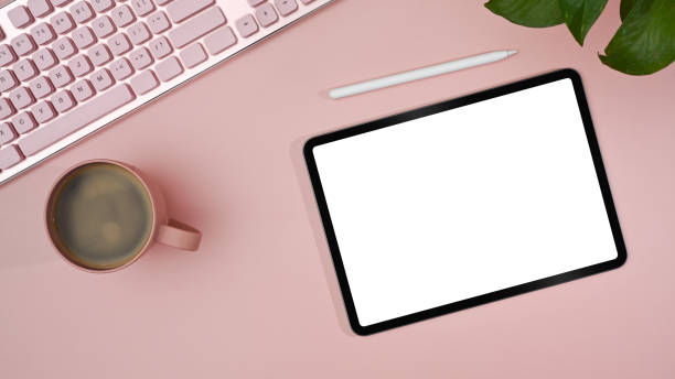 istock Top view digital tablet with empty display, stylus pen, coffee cup on pink background. Feminine workplace. 1411178255