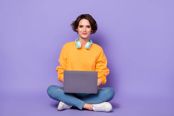 Full length photo of nice satisfied person sit use netbook write email coworking isolated on violet color background stock photo