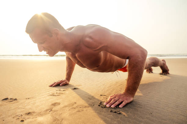 istock Muscular and fit young bodybuilder man doing workout warm up stretching on a paradise beach at sunset.fitness male model sport on sea 1411179886