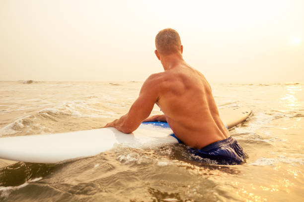 surfer fitness mann mit muskulösem körper mit seinem surfbrett am strand aufwärmen. - bali male beautiful ethnicity stock-fotos und bilder