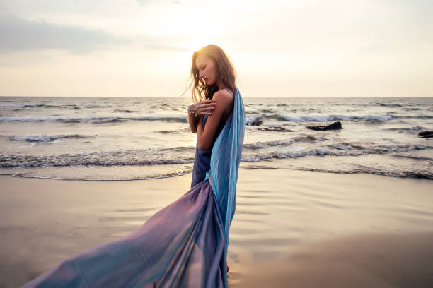 gorgeous style brunette young woman in blue chameleon dress long train standing on a rock near the sea, sand tropical on a rock.beautiful mermaid lonely melancholy waiting freedom and freelancing gorgeous style brunette young woman in blue chameleon dress long train standing on a rock near the sea, sand tropical on a rock.beautiful mermaid lonely melancholy waiting freedom and freelancing. goddess of ocean stock pictures, royalty-free photos & images