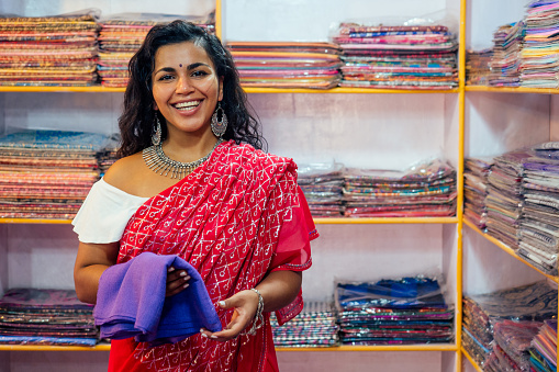 business lady in red traditional sari and jewelery clothes shop owner cashmere yak wool shawls.female seller in goa india arambol sale shop.designer seamstress tailor girl choosing fabric.