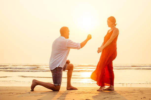 male making proposal with engagement ring to his girlfriend at sea beach.valentine's day february 14 wedding concept.man on his knee making a marriage proposal to his woman sunset romantic i said yes - day to sunset imagens e fotografias de stock