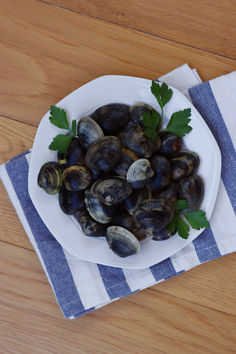 Raw fresh vongole clams with parsley on a plate om wooden table