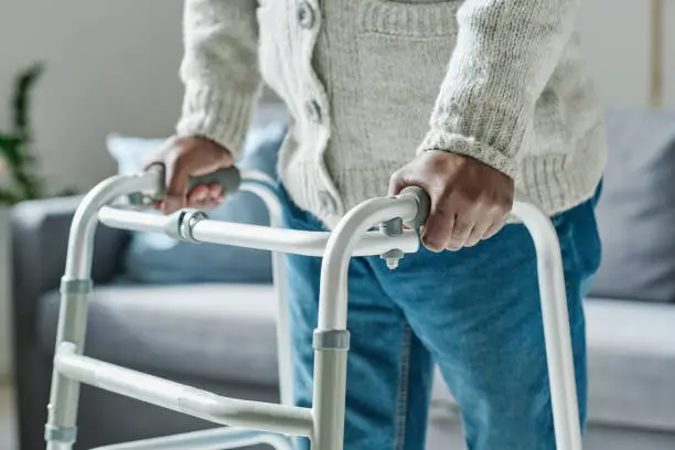 Close-up of African senior man with disability leaning on walker to move along the room