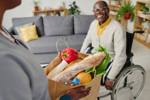 soignant livrant de la nourriture à un homme handicapé - women holding shopping bag living room photos et images de collection