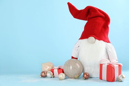 Cute Christmas gnome, gift boxes and festive balls on light blue background. Space for text