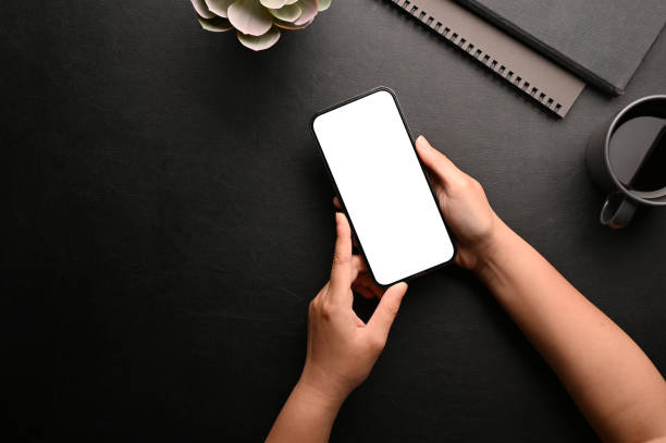 istock A female hands holding a smartphone white screen mockup over her modern black workspace. 1411184914