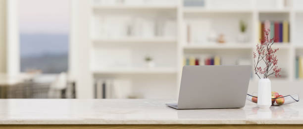 istock Minimal white marble tabletop with laptop and copy space against blurred home office in background. 1411185120
