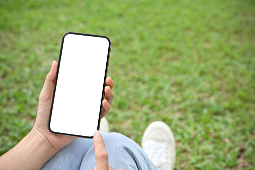 Close-up image, Female relaxes sit in the park and on her smartphone to chat with her friends. Mobile phone white screen mockup