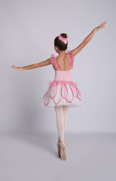 istock Beautifully dressed little ballerina dancing on grey background, back view 1411188738