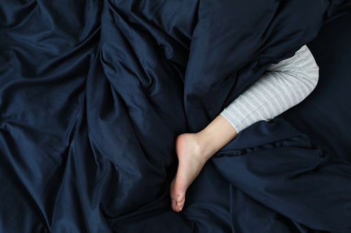 Woman sleeping in comfortable bed with dark blue linens, closeup of leg