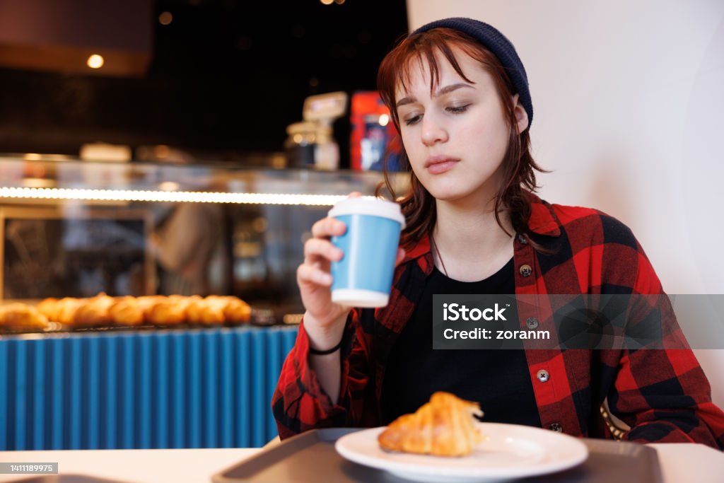 Teenage girl sitting in front of concession stand and having coffee in paper cup with pastry Teenage girl enjoying street food, siting in front of bakery counter and having coffee in paper cup with pastry 14-15 Years Stock Photo
