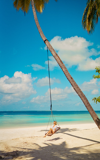 Beautiful woman sitting on rope swing with coconut palm tree