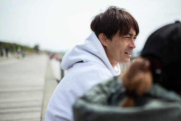Men and women standing on the beach terrace.\nTwo people is talking happily.\nThe sea on a sunny day.