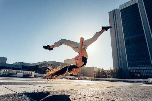 Young sportswoman performing a front flip outdoors in city. Female athlete practicing tricking against an urban background.