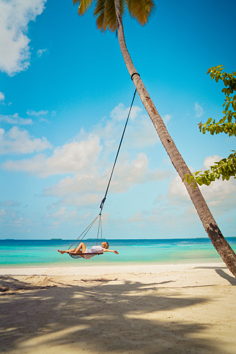 Beautiful woman sitting on rope swing with coconut palm tree