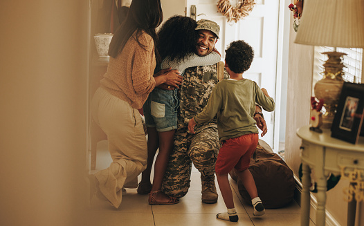 Heartwarming military homecoming. Happy soldier reuniting with his wife and children after serving in the army. Cheerful serviceman embracing his family after returning home from deployment.