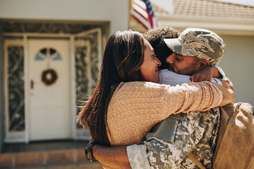 Military serviceman reuniting with his family after deployment. Soldier embracing his wife and daughter after returning from the army. Military man receiving a warm welcome from his family at home.