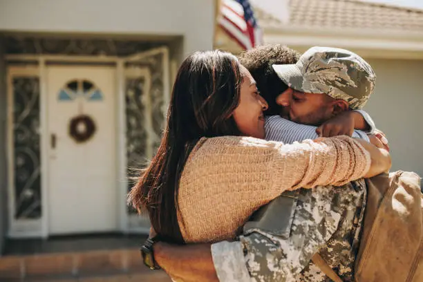 Military serviceman reuniting with his family after deployment. Soldier embracing his wife and daughter after returning from the army. Military man receiving a warm welcome from his family at home.