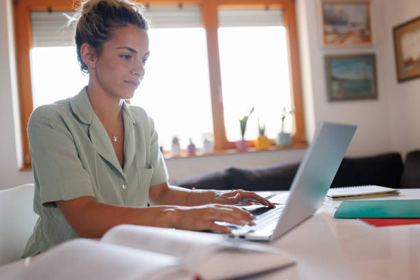 istock Beautiful young woman using laptop and studying at home 1411192410