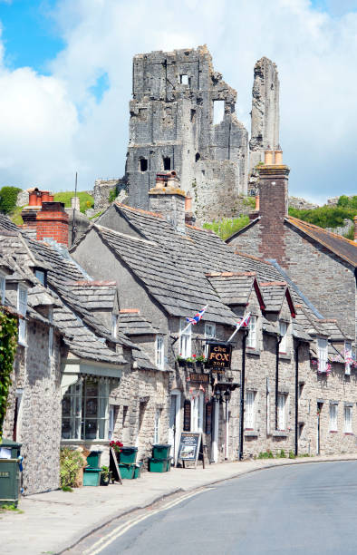 Corfe Castle ruins and cottages from West Street, Dorset, England. Summer in Britain brings out the colours of the countryside and sunlight lifts the hues and shades of natural stone and architecture in the quaint and tranquil villages of England