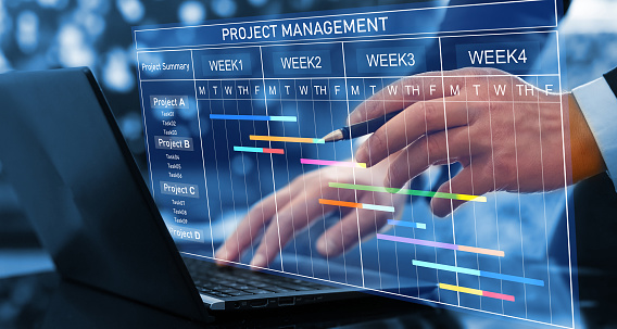 Project manager working on laptop and updating tasks and milestones progress planning with Gantt chart scheduling interface for company on virtual screen. Business Project Management System